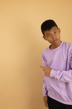 Kahverengi derili, eflatun kazak giyen genç bir Latin 'in dikey görüntüsü açık kahverengi bir arka planda parmaklarıyla fotokopi alanını gösteriyor.