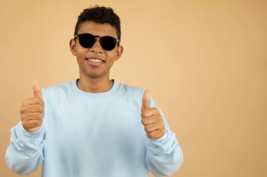 Koyu renk gözlüklü ve pastel mavi kazaklı gülümseyen Latin bir adam iki eliyle fotokopi çekilen açık kahverengi bir arka planda baş parmak hareketi yapıyor.