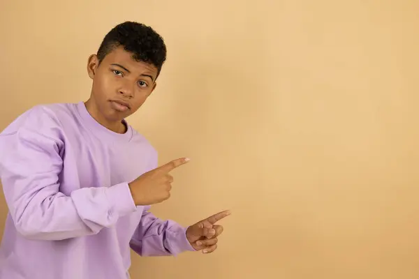 Genç, kahverengi tenli, eflatun tişörtlü bir adam açık kahverengi arka plandaki bir fotokopi alanını işaret ediyor. Reklam için reklam alanı.