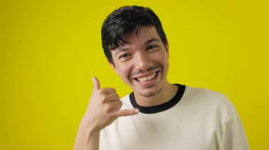 Çilli, neşeli bıyıklı genç bir adam, sarı arka plandaki fotokopi alanını işaret ederken telefonla jest yapıyor.