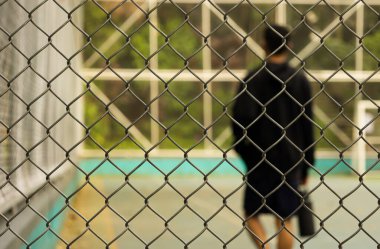 Odaklanmış metal örgüsü, arka planda bir parkta, açık hava sporunda dikkati dağılmış bir su şişesini tutan genç bir sporcuyla birlikte.