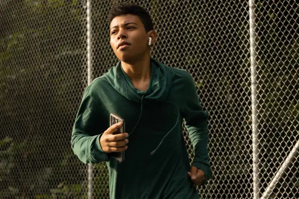 Sabahları çevresi doğa ile çevrili bir parkta koşan, kablosuz kulaklığı ve sağlıklı yaşam tarzıyla müzik dinleyen bir gencin alçak açısı.