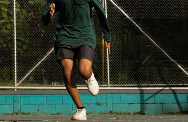 Tanınmaz haldeki Latin ergen sabahları parkta düz bir çizgide koşuyor, sabah güneşi alırken koşuyor, sağlıklı bir yaşam tarzı var.