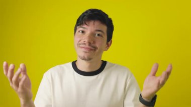 Neşeli çilli genç adam ellerini sarı bir arka planda tutarak soru sorup duruyor.