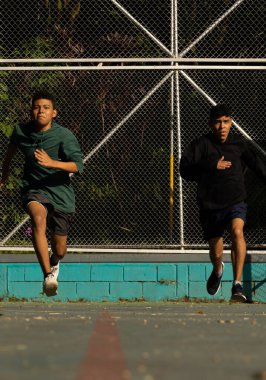 Güneşli bir günde sahada koşan koyu tenli iki Latin sporcu, sağlıklı bir yaşam tarzı.