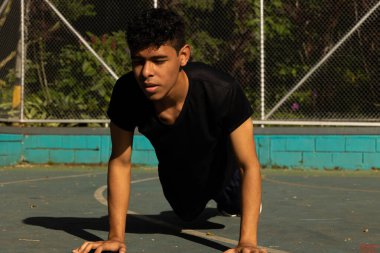 Genç esmer tenli atlet güneşli bir günde kortta şınav çekiyor, dışarıda egzersiz yapıyor.