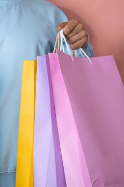 Mavi tulumlu bir adamın elinde pembe arka planda, alışveriş konsepti olan çok renkli alışveriş torbaları tutarken.