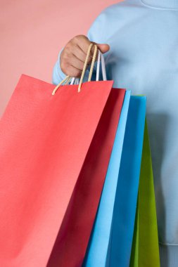 Mavi dalgıçlı bir adamın elinde pembe arka planda bir kaç renkli alışveriş torbası var.