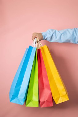 Mavi dalgıcın erkek eli pembe arka planda çok renkli alışveriş torbalarına bakıyor, tüketim kavramı.
