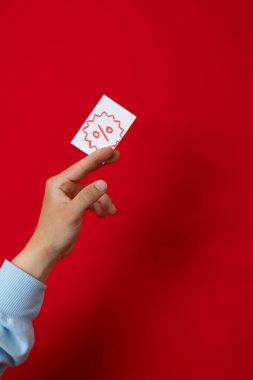 Kırmızı arka plan, indirim ve promosyon konseptinde indirim kartı tutan bir erkek.