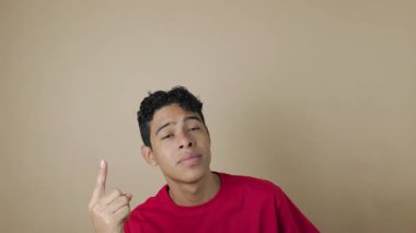 Kırmızı tişörtlü gülümseyen Latin bir adam açık kahverengi arka plan, reklam ve tanıtım konseptinin üstündeki bir fotokopi alanını işaret ediyor.