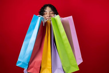 Elinde bir sürü renkli alışveriş torbası tutan genç bir kadın kırmızı arka plan, tüketim kavramı
