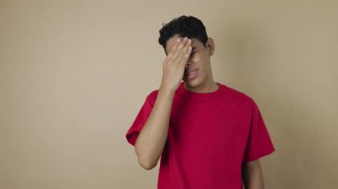 Kırmızı tişörtlü genç Latin bir adam, elleri ve gözleri açık kahverengi bir arka plan, endişe kavramı, hayal kırıklığı, gerilim ve sorunlar karşısında kapalı stresli