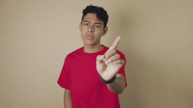 Genç Latin bir adam açık kahverengi bir arka planda inkar jesti olarak işaret parmağını sağa sola hareket ettiriyor. Reddetme, onaylama, uyarı ve kişisel sınır kavramı