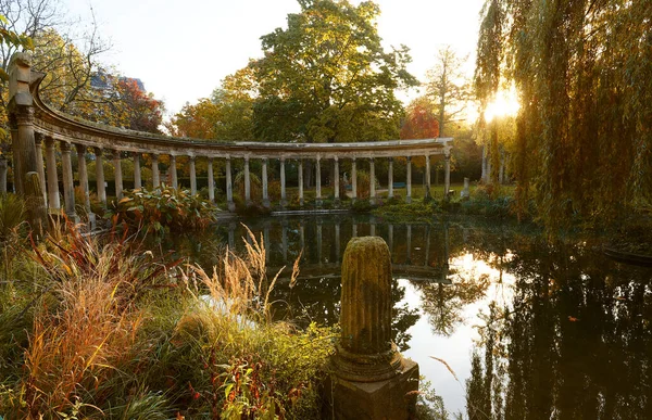 The ancient columns of Parc Monceau are reflected in the water of the oval basin, in the sun, in autumn . This public garden is located in the 8th district of Paris