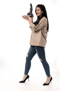 Kadın fotoğrafçı stüdyoda beyaz arka planda fotoğraf çekiyor, kot pantolon ve kahverengi deri ceket giyiyor. fotoğraf makinesi oturumu