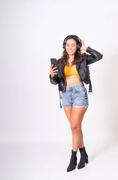 latin woman listening to music and dancing with high quality headphones on white background, jeans and leather jacket