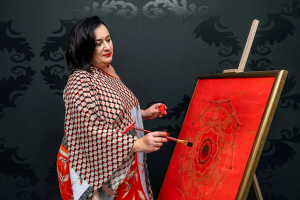 the artist draws a mandala with a brush and red paint on the canvas. High quality photo