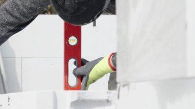 Evin duvarının inşaatı sırasında ruhsal bir seviyeyle tuğla yıkmak.