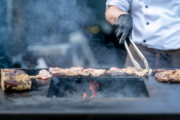 grilling meat for catering on an outdoor grill with an open fire, food street.