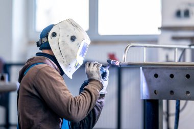 Bir mühendis, metal parçaları kaynaştırmak için kişisel koruyucu ekipman kullanıyor. Bu iş hassasiyet ve odaklanma gerektirir, iş ortamında güvenlik ve verimlilik sağlar.