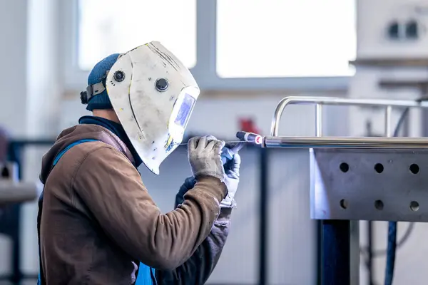 An engineering professional is using personal protective equipment to weld metal pieces together. This job requires precision and focus, ensuring safety and efficiency in the work environment
