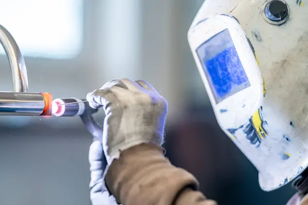 A man wearing a welding mask is using a machine to fuse a plastic pipe. The fluid inside is being connected for medical equipment using precise measuring instruments