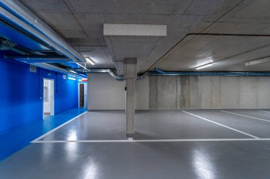 Mavi duvarlar, havalandırma boruları ve açık bir şekilde işaretlenmiş park alanları olan modern yeraltı otoparkı temiz ve düzenli bir ortam yaratıyor.