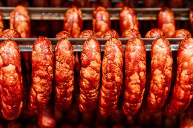 Rows of freshly smoked sausages are hanging on metal racks in a food processing factory, showcasing the industrial production of meat products clipart