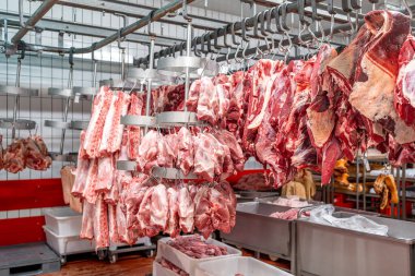 Kasaptaki metal kancalardan sarkan büyük domuz ve sığır eti parçaları satılık çeşitli et kesimlerini sergiliyor, bağışların tazeliğini ve kalitesini vurguluyor.
