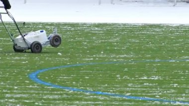 Bakım ekibi, bir futbol sahasındaki karı temizlemek için çizgi işaretleme makinesi kullanıyor. Oyun yüzeyinin kış koşullarına rağmen maça hazır olmasını sağlıyor.