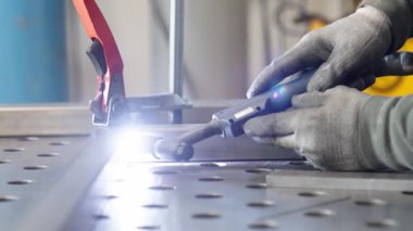 Yetenekli kaynakçı titizlikle kaynak masasındaki metal bileşenleri birleştirir. Güçlü ve kusursuz bir bağlantı kurmak için kaynak makinesini ustalıkla kullanır.