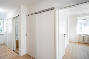 Beyaz sürgülü kapılar modern bir dairedeki odaları ayırıyor, ahşap zeminli minimalist iç tasarımı sergiliyor ve geniş doğal ışık bir boşluk ve sükunet hissi yaratıyor.