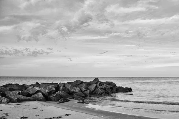 黒と白で撮影された空に雲とデンマークの海に突き出た石のグロイン デンマークの海岸風景 海からの風景写真 — ストック写真