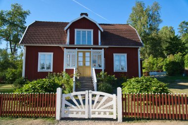 Smalland 'daki İsveç kırmızı beyaz geleneksel evi, beyaz çit yeşil bahçe mavi gökyüzü. İsveç 'teki tatillerden kalan çocukluk anıları. İskandinav manzarasından doğa fotoğrafı.
