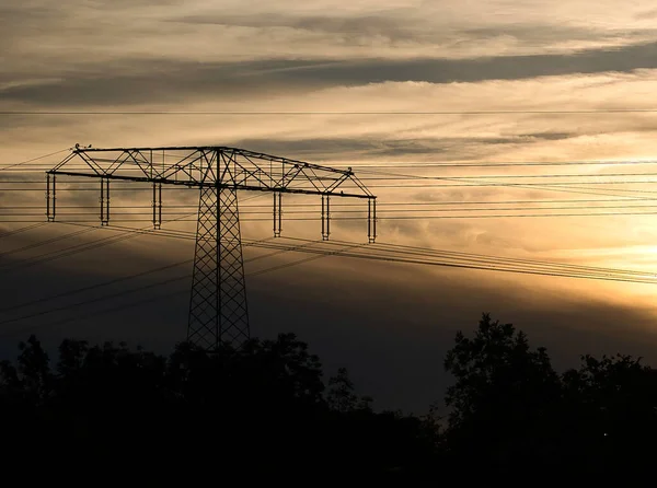 High-voltage power pole with overhead line through which the electricity is transported. Partial grid supplier to the sunset. Technical industry image from nature