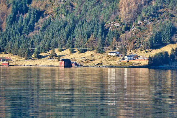 有山峦在地平线上的峡湾 海岸上石头 树木和草地之间的小房子 挪威的水在阳光下闪闪发光 北部的风景照片 — 图库照片