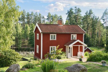 a typical red and white swedish house in smalland. green meadow in foreground, small forest in background. Blue sky with small clouds. Scandinavia landscape photo clipart