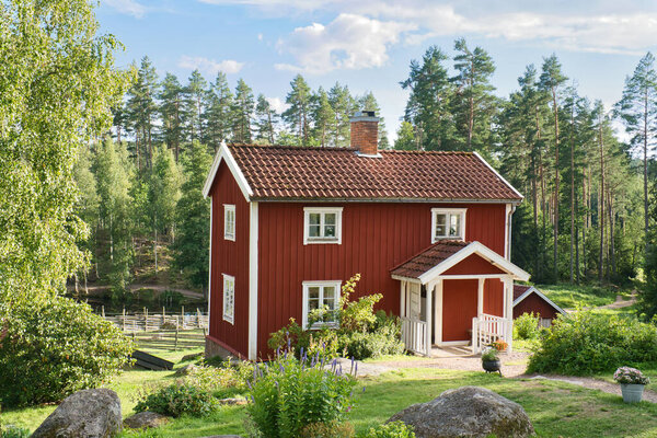a typical red and white swedish house in smalland. green meadow in foreground, small forest in background. Blue sky with small clouds. Scandinavia landscape photo