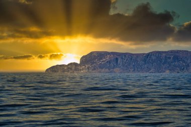 Norveç 'in batısındaki deniz manzarası. Güneş ışığı ve ağır bulutlar. Ön planda dalgalar, arka planda kayalar. Avrupa 'nın en batı noktası