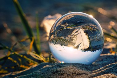 Zingst 'teki Baltık Denizi sahilinde, topun içinde manzaralı bir tüy tasvir edilmiş cam top. Günbatımı sıcak bir ışık sağlıyor.
