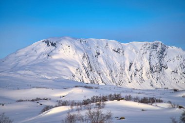 Norwegian high mountains in the snow. Mountains covered with snow. Snow-covered landscape in Scandinavia clipart