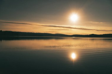 Sunrise over a Swedish lake with mirror-smooth water in front of trees on the shore. Nature shot from Scandinavia clipart