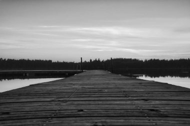 İsveç gölünde gün batımında ahşap iskelede. Siyah-beyaz çekilmiş. İskandinav topraklarında yıkanan bir göl