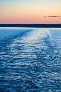Gün batımında denizdeki bir adadan kalkan bir geminin görüntüsü. İskandinav doğası