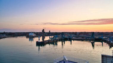 The harbor of Trelleborg, Sweden, at sunrise with calm water, blue harbor facilities and a city view in the background. clipart