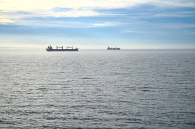 İki kargo gemisi berrak bir gökyüzünün altında sakin bir denizde süzülüyor. Uçsuz bucaksız denizcilik, ulaşım ve deniz sükunetine odaklı minimalist bir atmosfer..