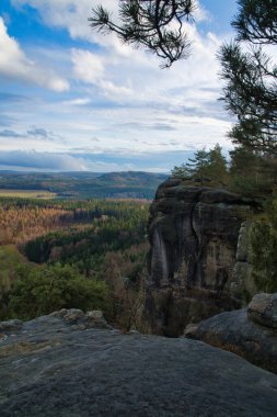 Görkemli kaya oluşumu, mavi gökyüzünün altındaki ormanlık bir vadinin üzerinde yükseliyor. Macera, doğa ve seyahat tutkusu için mükemmel bir zemin.