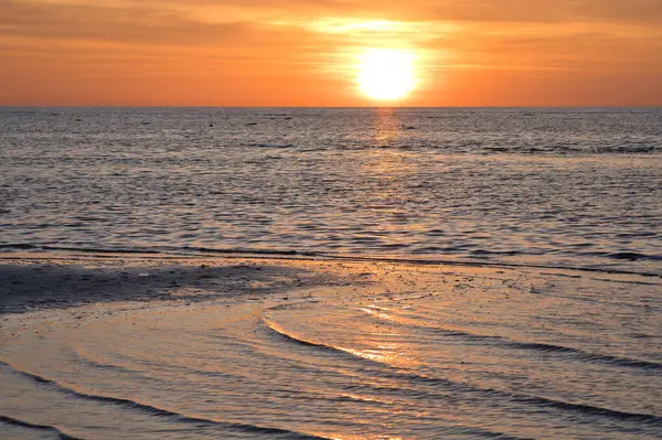 Sakin okyanusun üzerinde sıcak gün batımı, altın yansıma ve nazik dalgalar, huzurlu ruh hali ve doğal renk çeşitliliği ile.