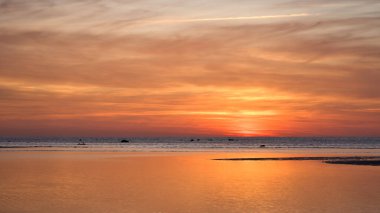 Sakin okyanusun üzerinde sıcak gün batımı, altın yansıma ve nazik dalgalar, huzurlu ruh hali ve doğal renk çeşitliliği ile.
